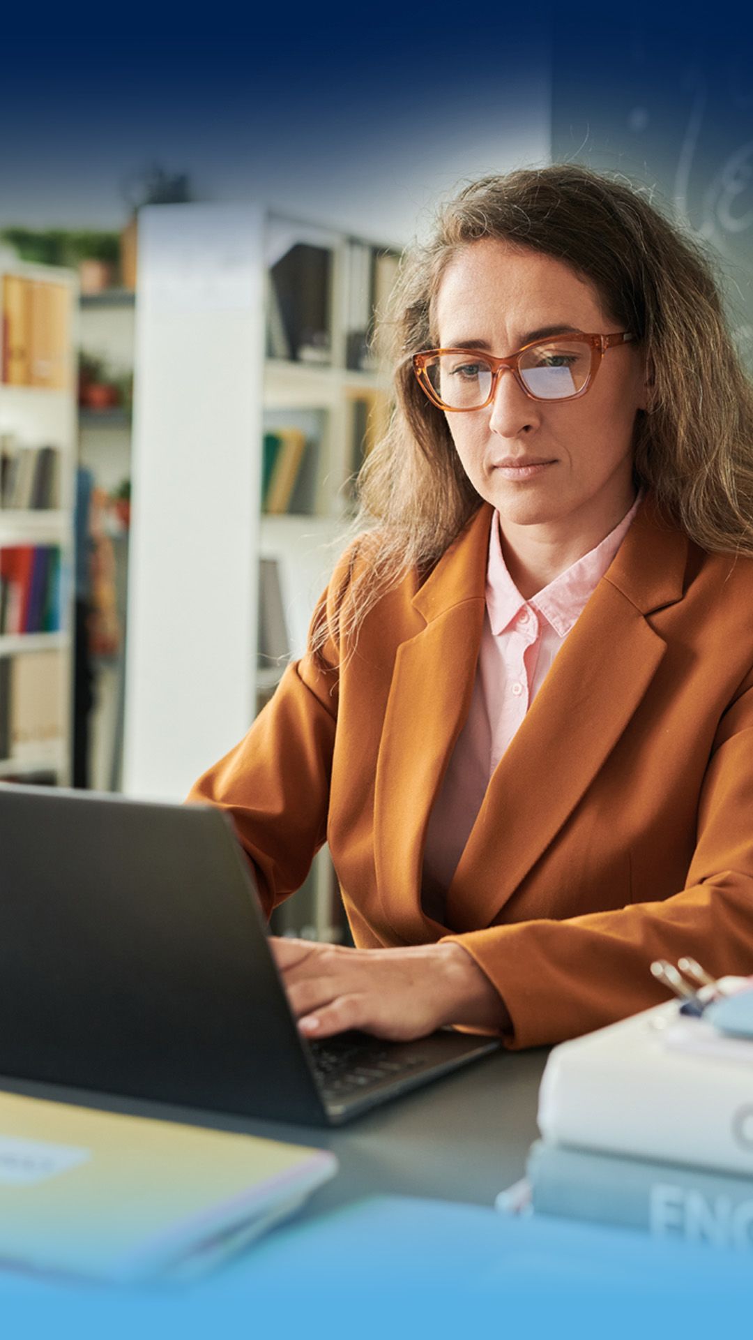 Female teacher in classroom looking anxious while viewing a laptop screen.