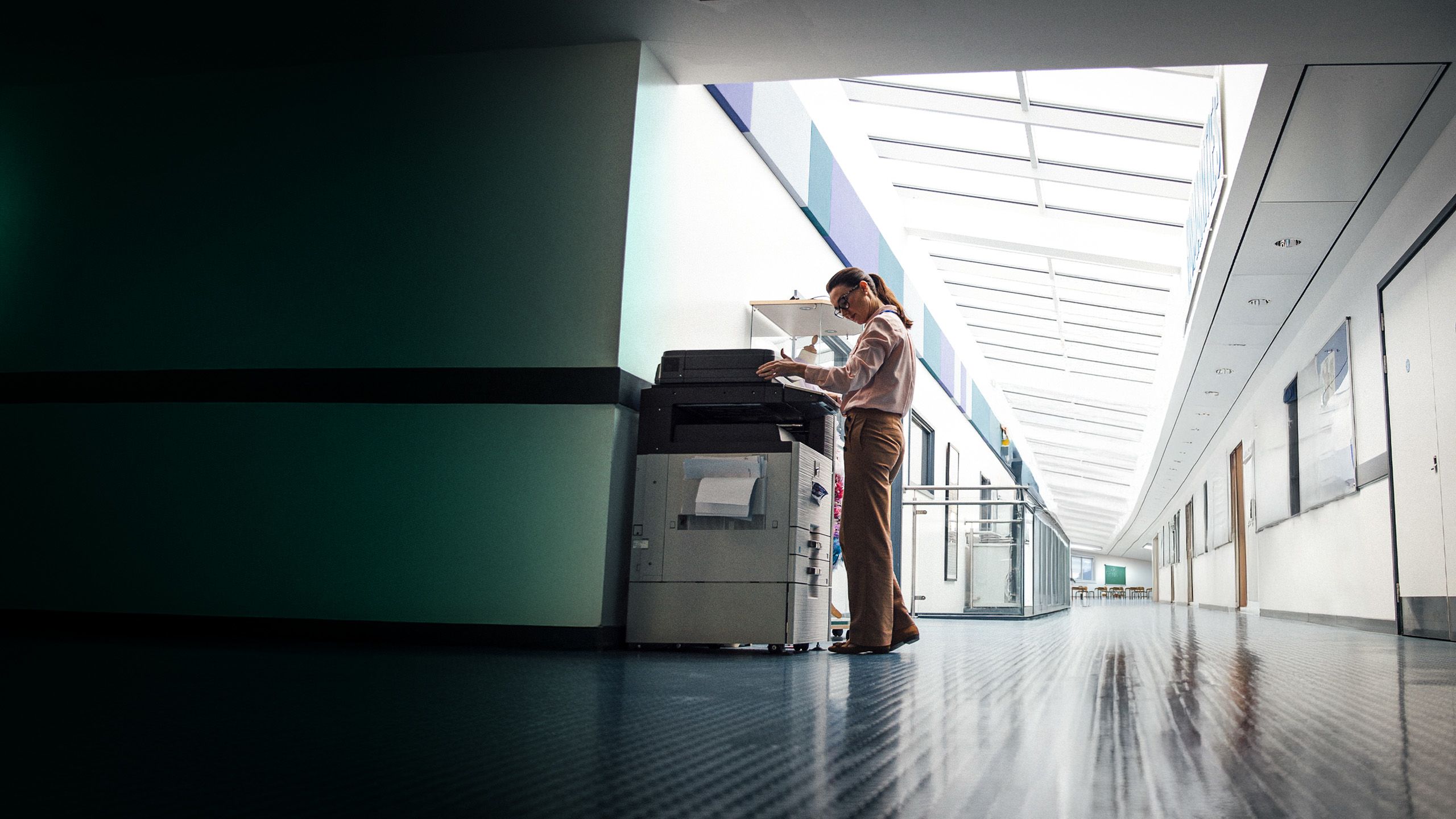 Teacher using a photocopier in a school hallway.