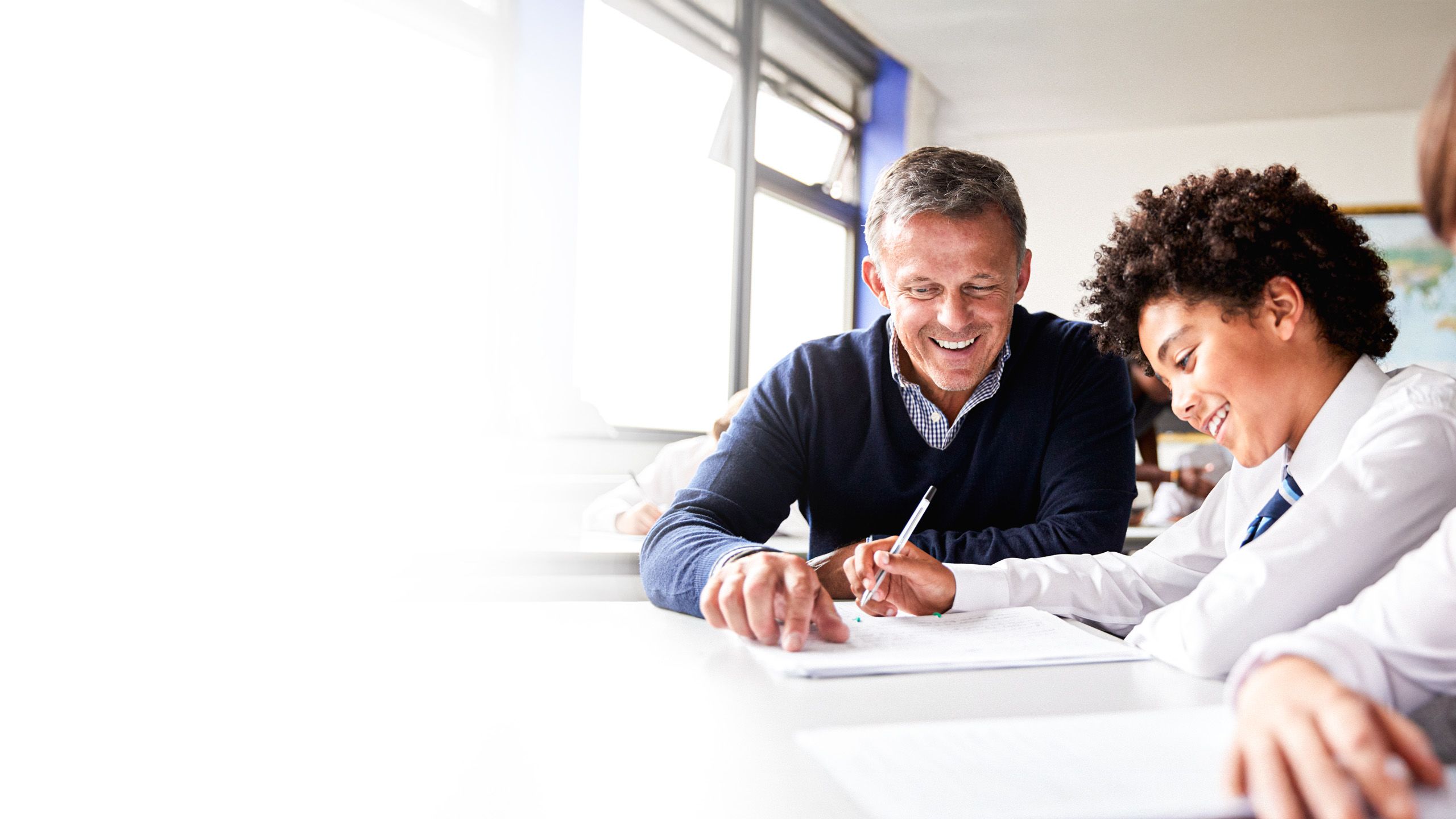 Teacher and student sitting together at a desk, smiling as they go through schoolwork.