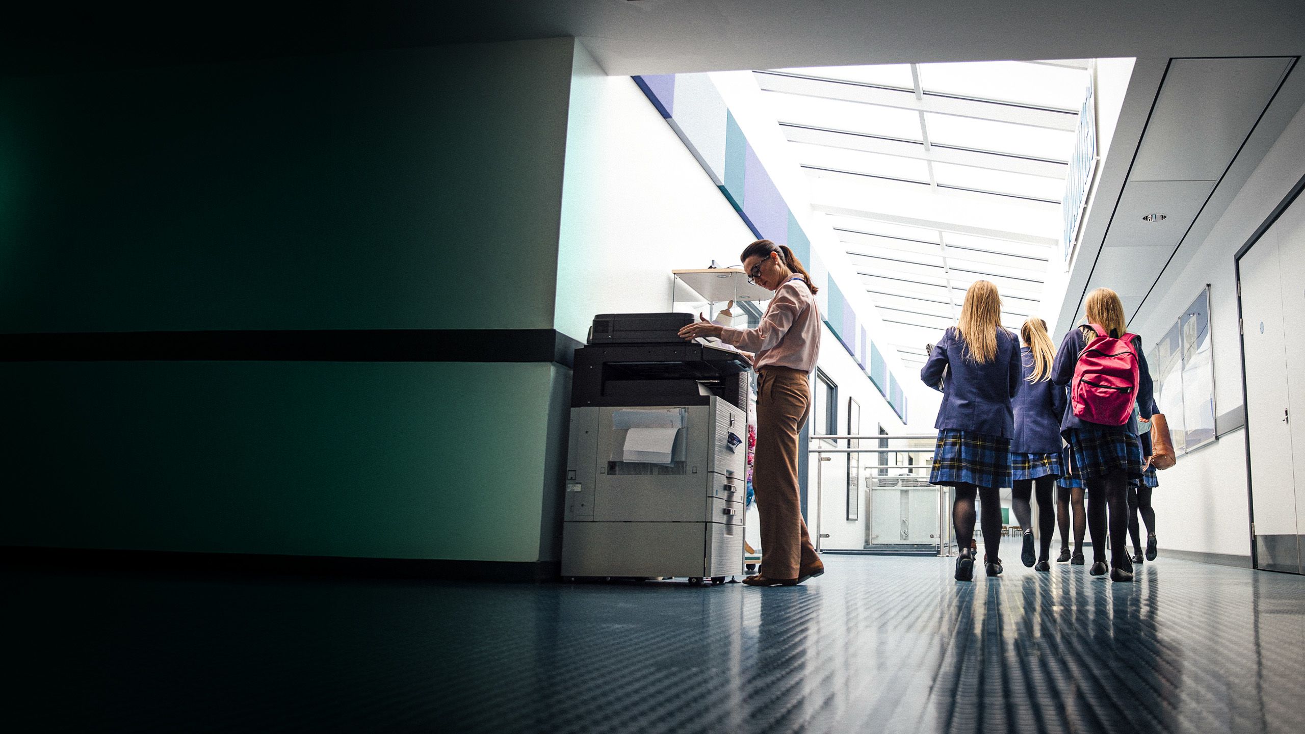Teacher using a photocopier in a school hallway.