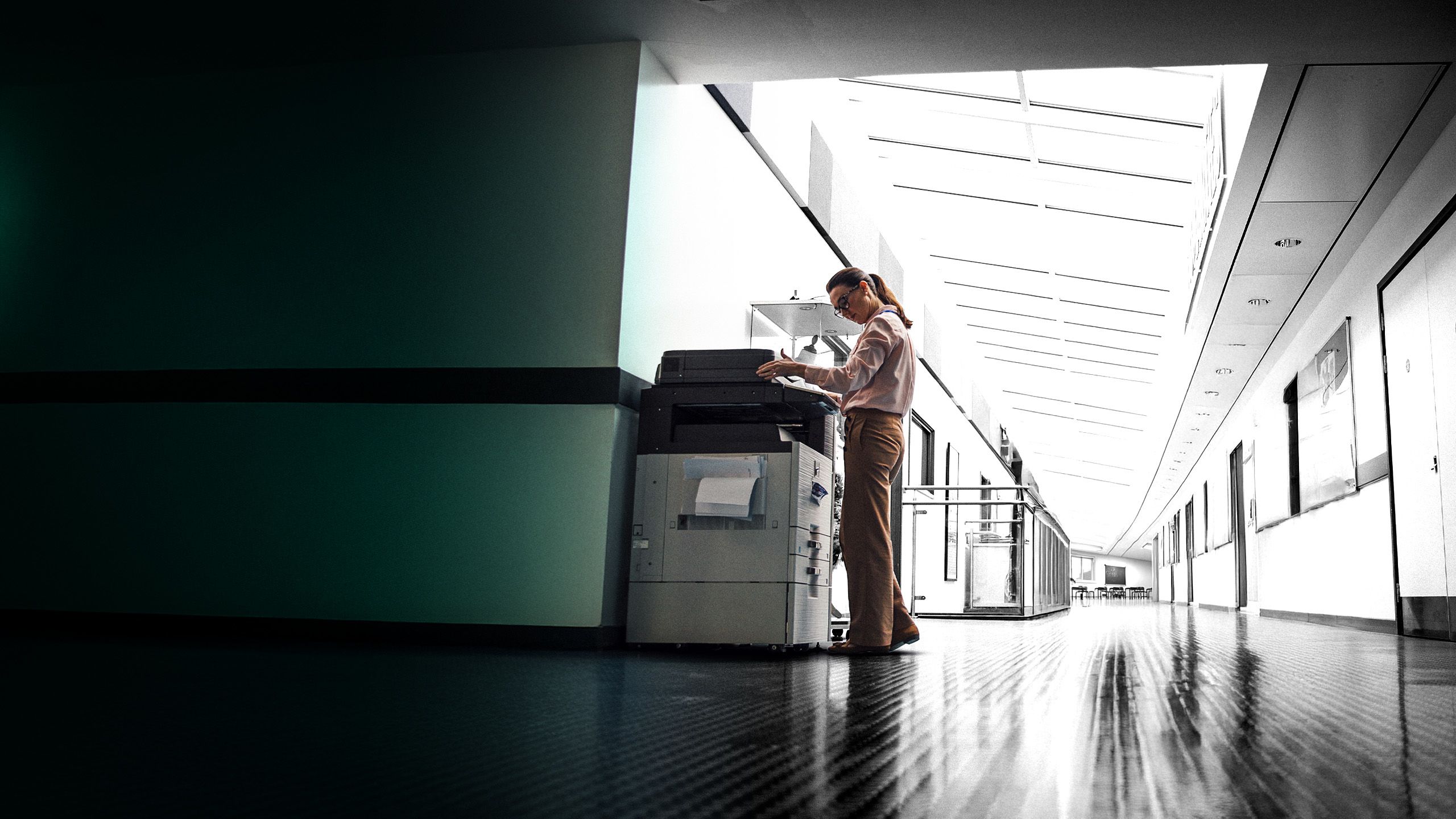 Teacher using a photocopier in a school hallway.