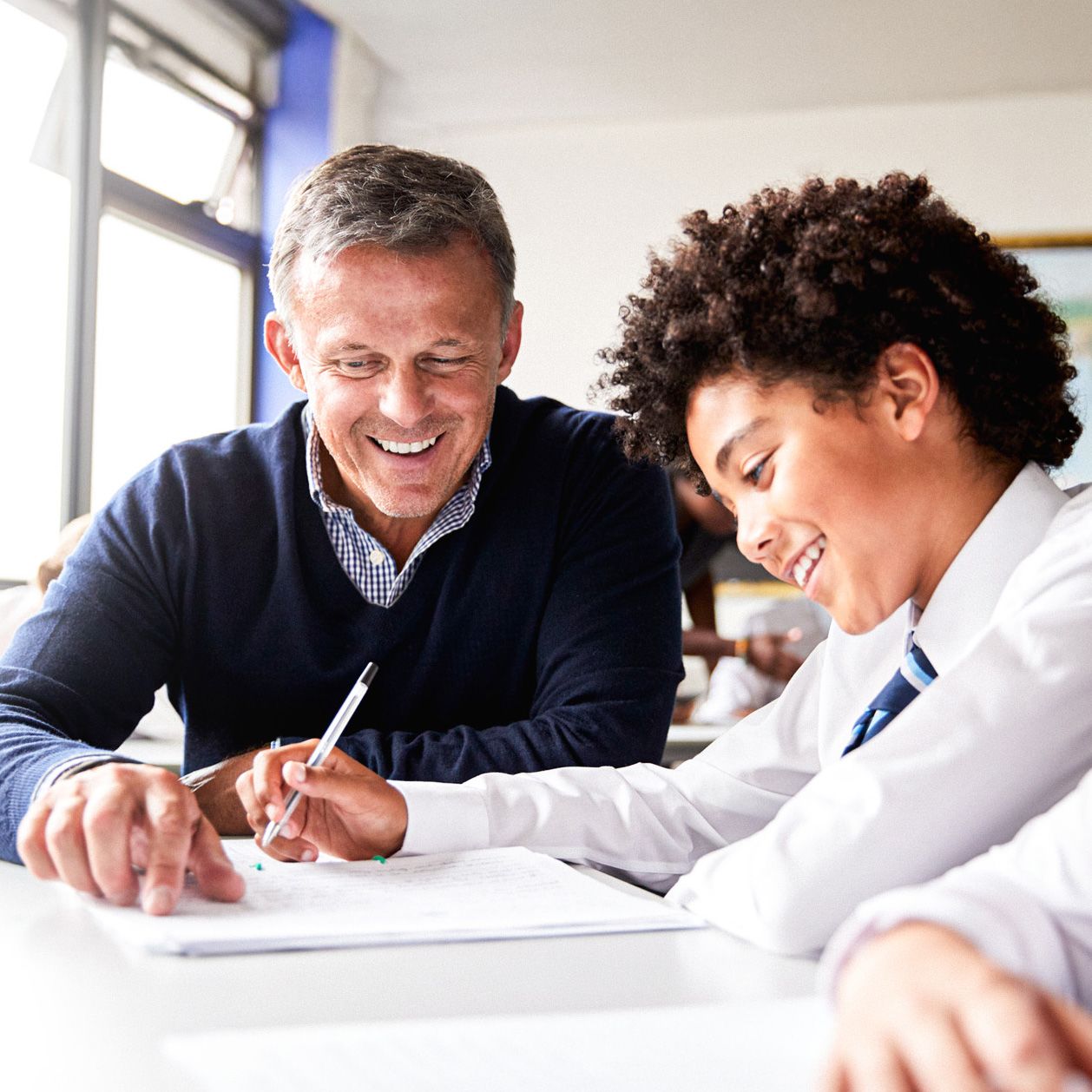 Teacher and student sitting together at a desk, smiling as they go through schoolwork.